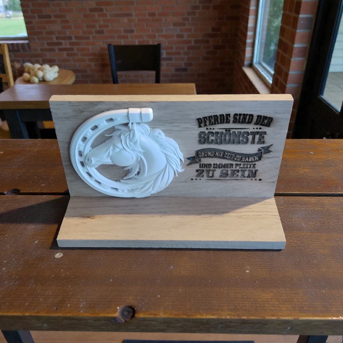 Ein Pferdekopf im Hufeisen aus Keramik mit Holzrahmen und Gravur