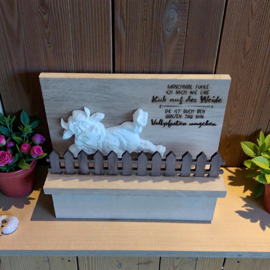 Eine Kuh aus Keramikguss auf Holz mit Vollpfostenspruch