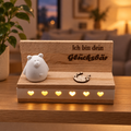 Glücksbär mit beleuchtetem Holzsockel auf einem Regal im Wohnraum