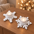 Zwei weiße Schneeflockenhalter aus Keramikguss mit LED-Teelichtern auf einem Holzsideboard